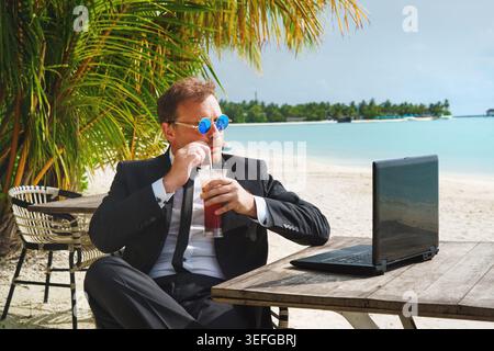 Remote online working on summer beach. A businessman with a laptop is conducting an online conference from a tropical island. Stock Photo