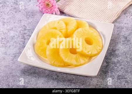 Vibrant yellow pineapple slices in light syrup, arranged neatly on clean white rectangular plate. Soft, natural light illuminates juicy texture Stock Photo