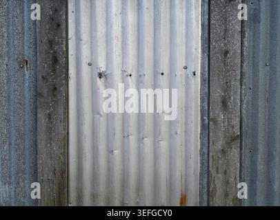 Overlapping reclaimed corrugated tin panels with white painted and blue tinted metal surfaces, vertical weathered wood boards Stock Photo