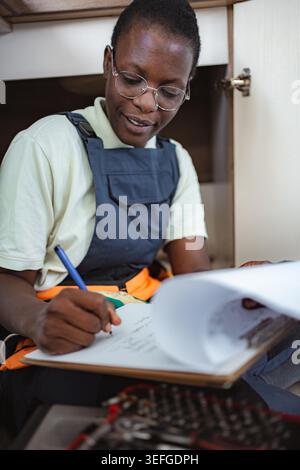 Smiling african american female plumber writing notes on her clipboard Stock Photo