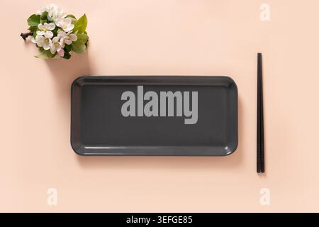 Empty rectangular gray plate for asian food with black chopsticks on pink background surface with spring branches. Asian style. View from above. Copy space. Japanese food concept. Stock Photo