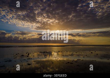 Aerial view of the sun setting over a calm lagoon with dramatic sun rays piercing through a cloudy sky and reflecting on the water surface Moka Distri Stock Photo
