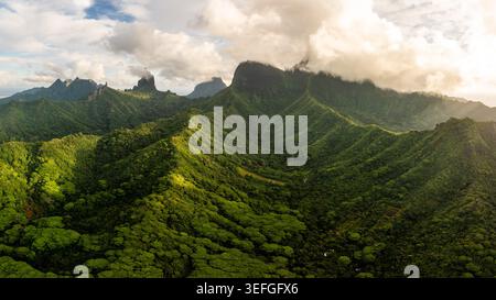 Aerial view of the lush volcanic peaks of Moorea and dense tropical forests under a cloudy sky in Moorea-Maiao, Windward Islands, French Polynesia. Stock Photo
