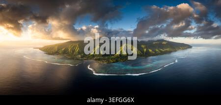 Aerial view of the lush volcanic peaks and turquoise lagoon of Moorea under dramatic sunset clouds Moorea-Maiao, Windward Islands, French Polynesia. Stock Photo