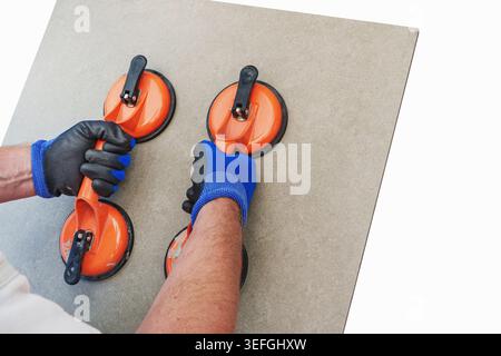 A construction worker holds a ceramic tile with a suction cup lifter, isolated against a free PNG background. Concept for laying ceramic tiles. Stock Photo