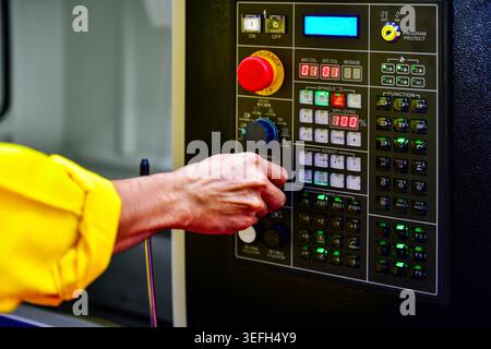 Operator hand adjusting dial knob on CNC machine control panel, industrial manufacturing concept. Stock Photo