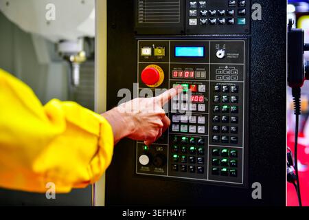 Operator hand pressing button on CNC machine control panel, industrial manufacturing process Stock Photo