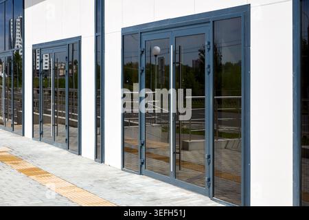 Dark gray aluminum double doors with large glass panels installed in white building facade. Modern architectural design features long vertical handles Stock Photo