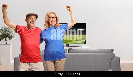 Happy mature couple cheering and watching a football match on tv Stock Photo