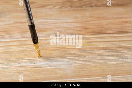 A screwdriver screws a screw into a wooden surface in close-up. Carpentry, repair or furniture assembly concept Stock Photo