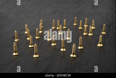 Yellow metal screws pile. Gold bolts close up, industry hardware macro texture, golden screw on black background Stock Photo