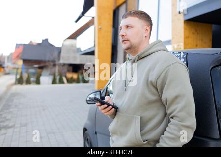 Man using smartphone standing near car outdoors Stock Photo