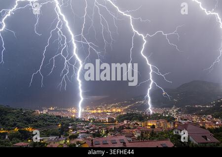 View of powerful lightning bolts striking over the city skyline and rooftops at night in La Spezia, Liguria, Italy. Stock Photo