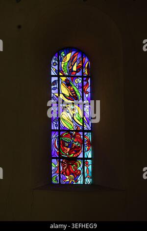 View of a colorful abstract stained glass window inside Ribe Cathedral with vibrant light filtering through the dark stone wall Ribe, Denmark. Stock Photo