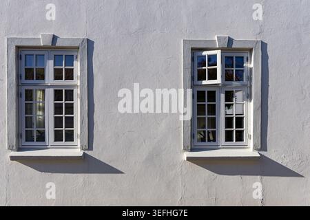 View of two white-framed windows on a textured facade with sharp shadows in Ribe, Denmark. Stock Photo