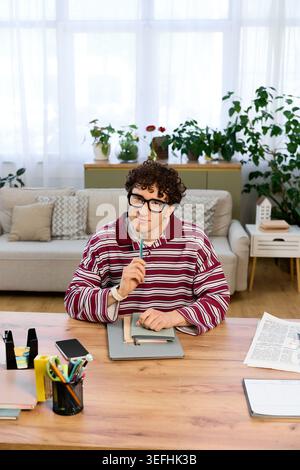 Young man with curly hair relaxes in his stylish apartment while brainstorming ideas. Stock Photo