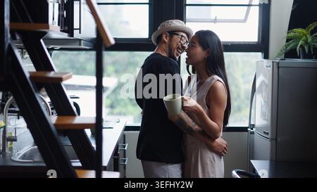 Happy diverse couple embracing in kitchen at home, enjoying morning coffee together Stock Photo