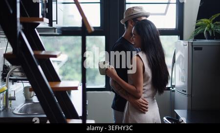 Young couple hugging in modern home kitchen, sharing relaxed intimate moment Stock Photo