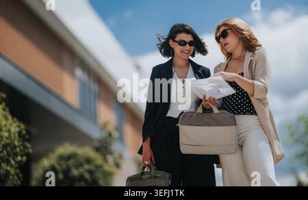 Two businesswomen discussing documents outdoors after a meeting near modern office building Stock Photo