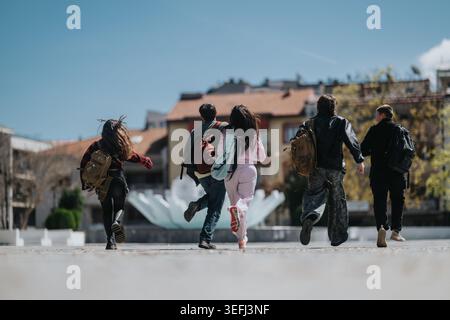 School friends running together across a city square with backpacks and casual clothes Stock Photo