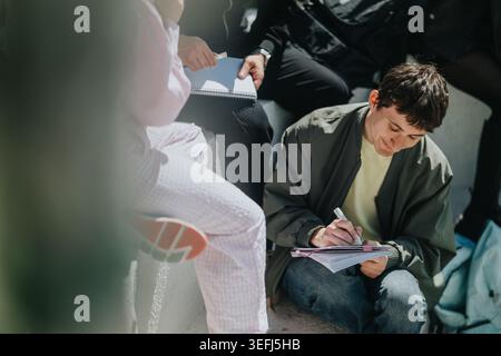 High school students studying and writing together outdoors during a casual group study session Stock Photo