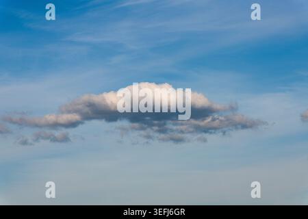 Beautiful fluffy white cloud isolated on a clear blue sky background with soft golden hour light. Simple and peaceful nature landscape. Stock Photo