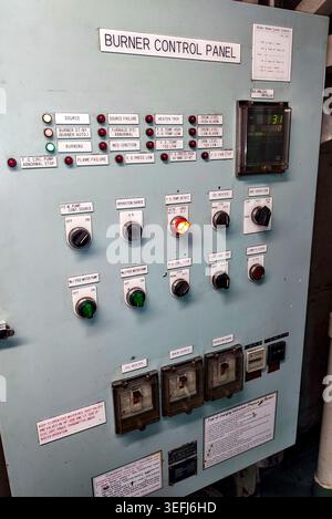 Front view of a vintage metal marine boiler control panel featuring analog toggle switches and round indicator lights. Stock Photo