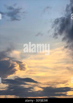 Soft layered sunset clouds spreading across evening sky with warm golden light. Atmospheric weather background featuring textured cloud formations and Stock Photo