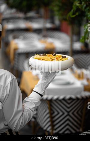 Waiter serving gourmet pasta in white bowl Stock Photo