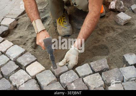 Italy, Worker Using Hammer to Laying Pavement, Manual Laying of Porphyry Cubes on the Road Stock Photo