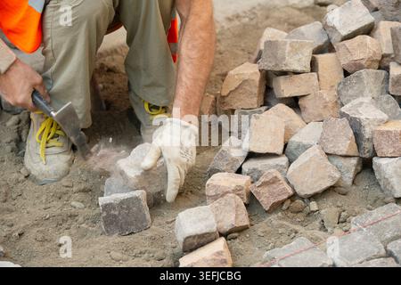 Italy, Worker Using Hammer to Laying Pavement, Manual Laying of Porphyry Cubes on the Road Stock Photo