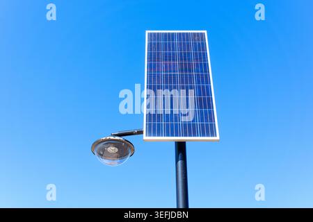 Solar street lamp features a photovoltaic panel and round glass lantern fixture mounted on a black pole, providing sustainable outdoor lighting soluti Stock Photo