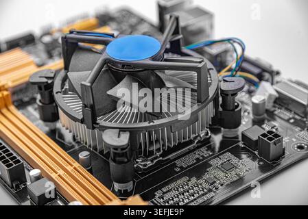 CPU cooler mounted on a black and orange computer motherboard. Stock Photo