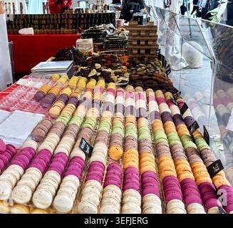 Display of colorful French macarons and chocolate sweet on a stall at an outdoor food festival, artisanal pastry market background. Stock Photo