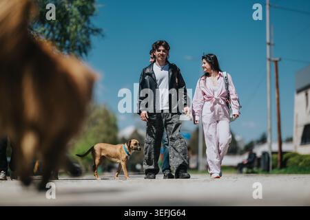 School friends walking together with dogs on a sunny urban street holding hands and smiling Stock Photo