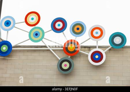 Abstract Wall Installation at Oshawa Art Exhibition Gallery, A vibrant circular abstract installation mounted on a beige brick wall Stock Photo