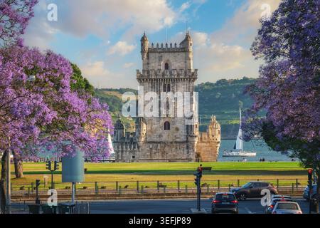 View of Belem Tower surrounded by beautiful purple jacaranda flowers on the Tagus River during sunset in Lisbon. Belem, Lisbon, Portugal Stock Photo