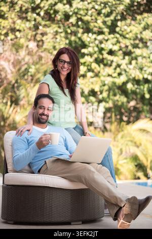 Middle Eastern couple relaxing outdoors with laptop and coffee, modern Arab family lifestyle portrait Stock Photo