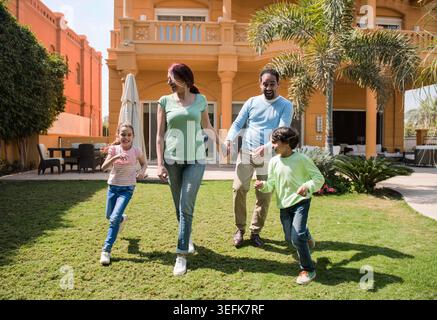 Happy family walking and playing together in a sunny villa garden holding hands Stock Photo