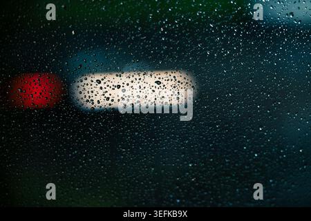 Raindrops on a window glass window at night with blurry car headlights and taillights bokeh on the background. Stock Photo