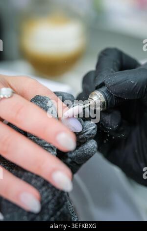 Precision manicure image of a rotating nail drill shaping the surface of a long almond nail while dust gathers on gloved hands. Stock Photo