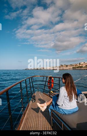 Woman sits quietly on boat's deck, gazing at calm sea Stock Photo