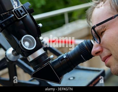 Person looking through an astronomical telescope eyepiece, illustrating hands on optical exploration while learning the sky. Stock Photo