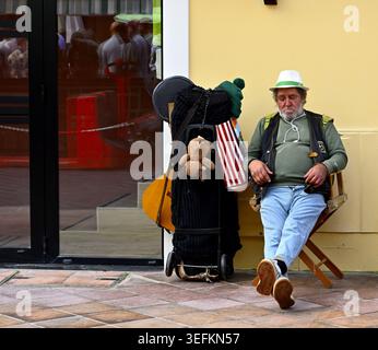 Man relaxing on char next to wall outside next to trolley of possessions Stock Photo