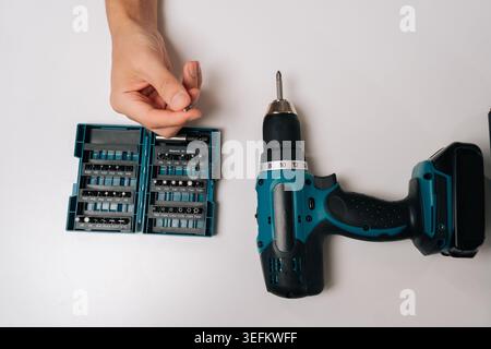 Top view of person selecting bit from comprehensive driver bit set, preparing to use cordless electric power drill for upcoming diy project or home Stock Photo