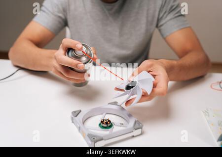 Cropped shot of repairman lubricating computer cooling fan blade and base with aerosol sprayer, performing essential maintenance for system cooling Stock Photo