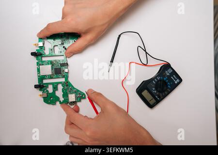 Electrician hands testing game controller circuit board with multimeter, troubleshooting electronic components and diagnosing issues during repair and Stock Photo