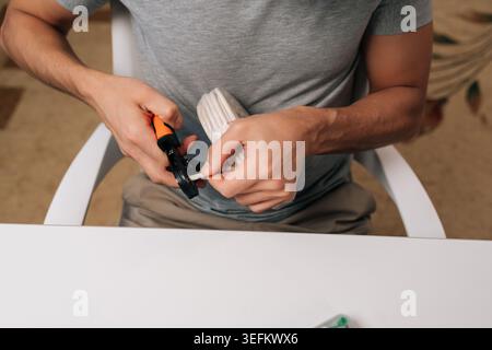 Close-up of electrician hands holding cable crimping tool, preparing white electrical wire for secure connection, performing precise task of Stock Photo