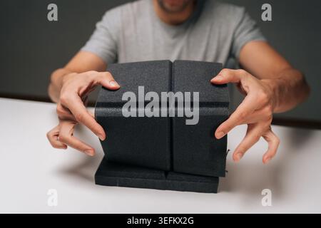 Close-up of man holding black acoustic foam panel, examining sound absorbing material for noise control, soundproofing, insulation in dark recording Stock Photo
