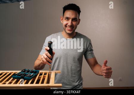 Portrait of cheerful man installing and building wooden furniture components with electric screwdriver, showcasing successful home assembly and Stock Photo